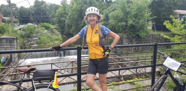 Woman on a bike tour standing alone in bicycling wardrobe and helmet on a bridge