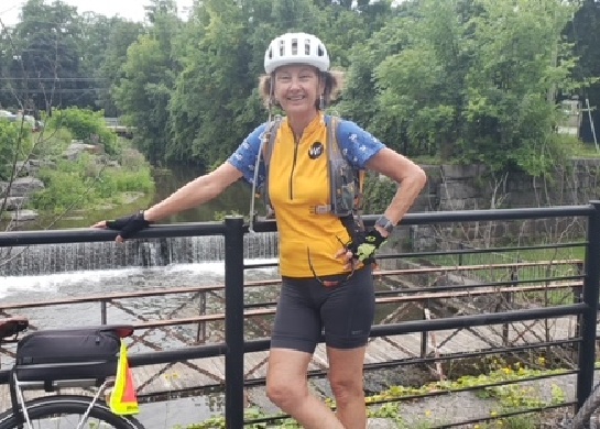 Woman on a bike tour standing alone in bicycling wardrobe and helmet on a bridge